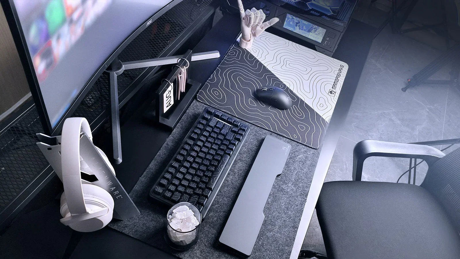 A modern, monochromatic gaming desk setup with a curved monitor, mechanical keyboard, white headphones, and a topographic mousepad