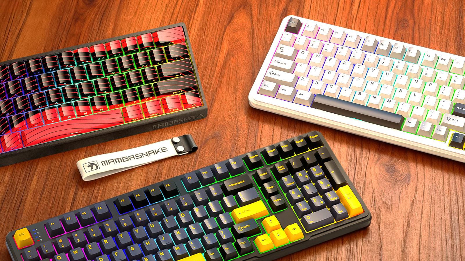 Three colorful Mambasnake mechanical keyboards with RGB lighting, featuring different designs, displayed on a wooden desk