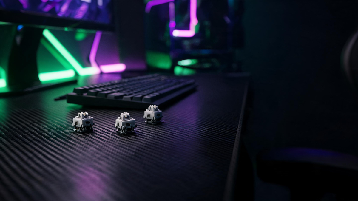 Silent mechanical switch samples beside a compact keyboard on a dark gaming desk with vivid RGB lighting and open space for a headline