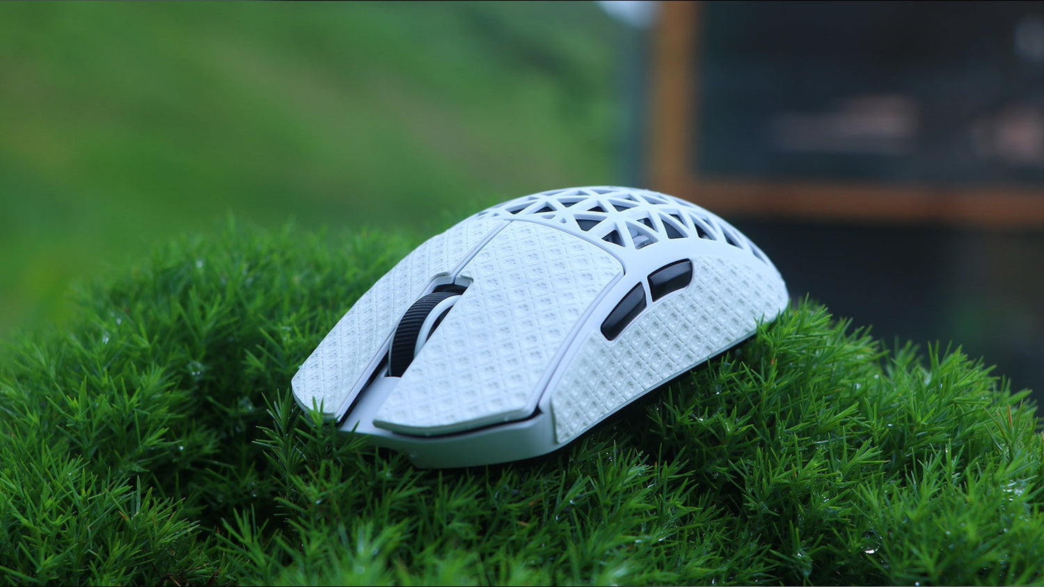 A close-up of a white gaming mouse with a textured, honeycomb-like shell, resting on a bed of vibrant green moss or grass