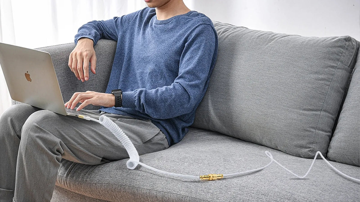 Man using laptop with white coiled aviator USB‑C keyboard data cable on sofa