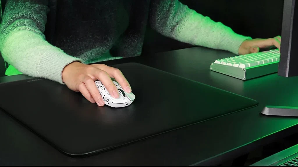 Hand using a white perforated mouse on a dark desk under green lighting.