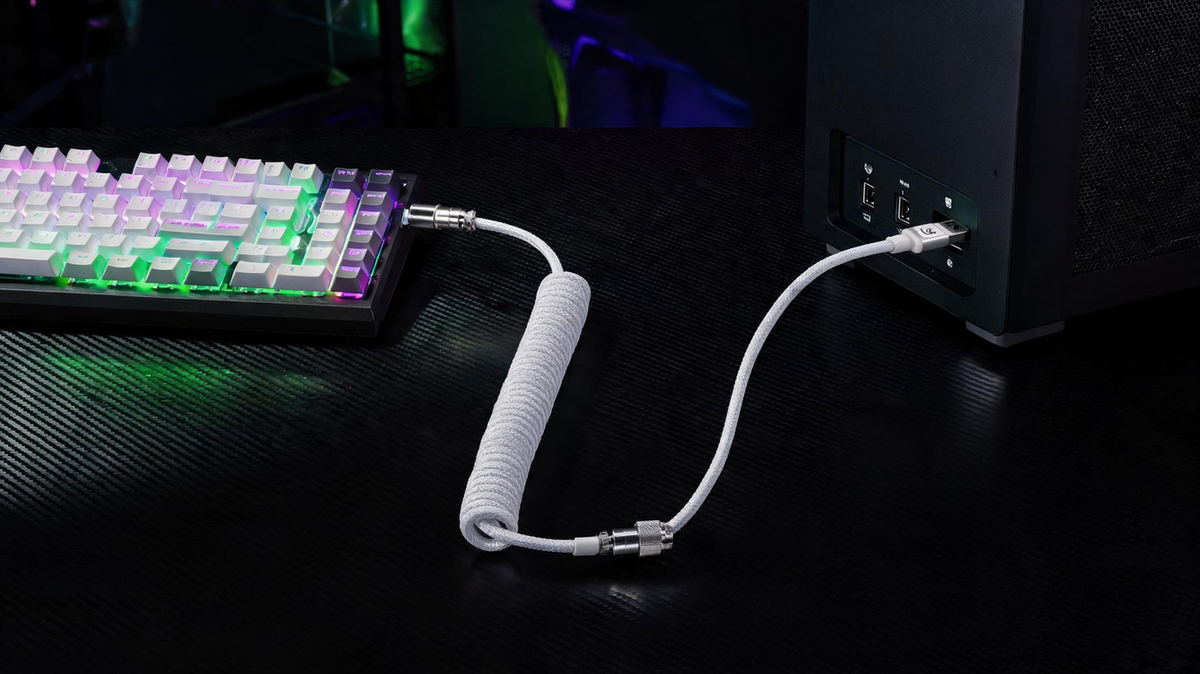 White coiled aviator keyboard cable arranged beside a mechanical keyboard on a carbon-fiber gaming desk with purple and neon-green RGB lighting