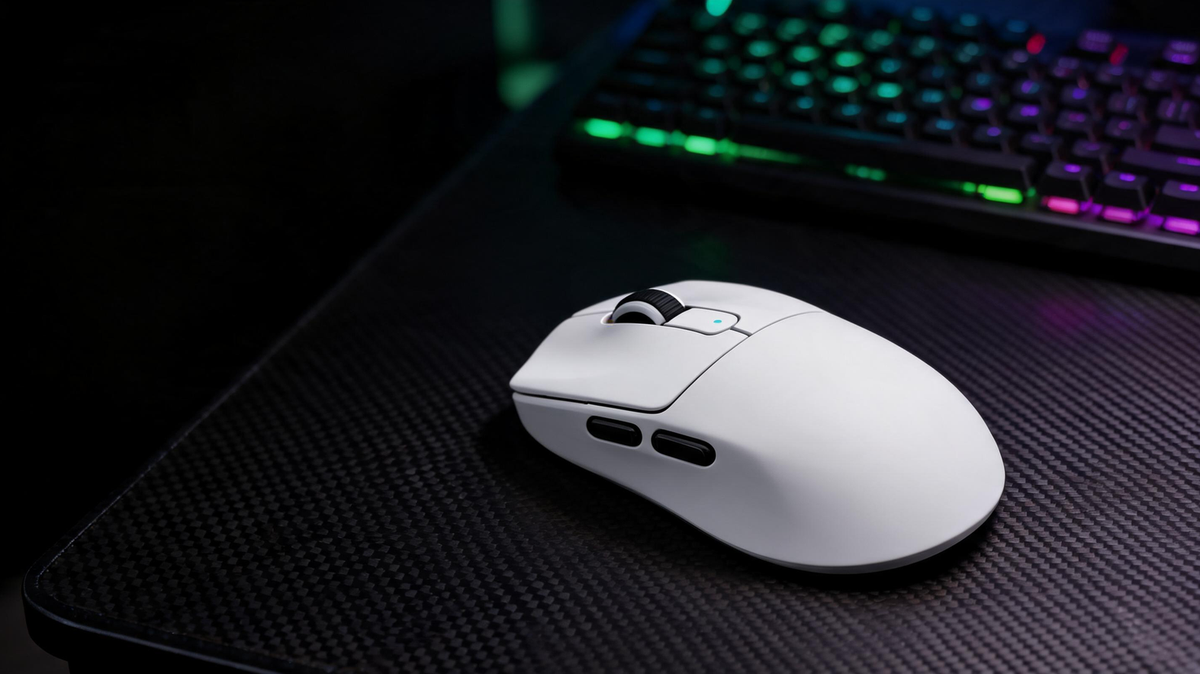 Wireless gaming mouse resting on a carbon-fiber gaming desk beside a glowing monitor setup