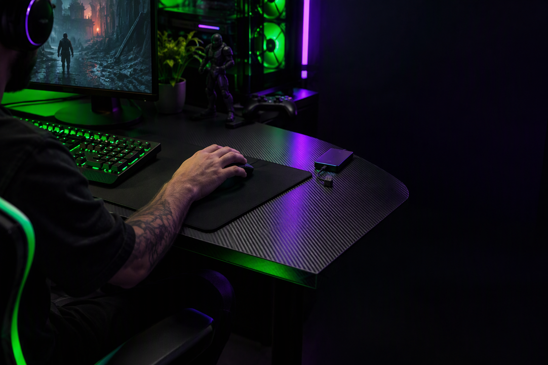 A wireless mouse and its USB receiver beside an external drive on a neon-lit gaming desk.