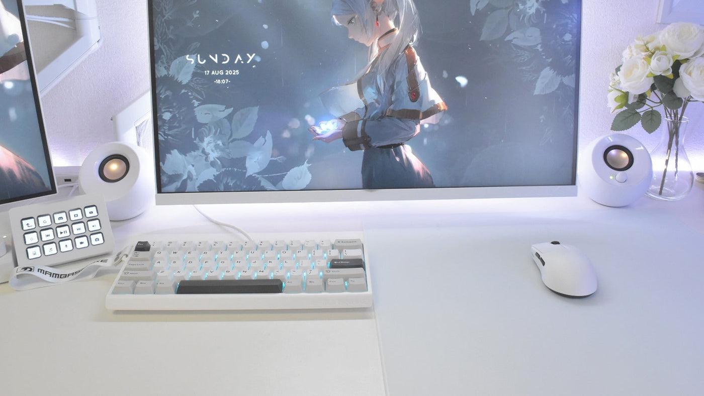 Clean white gaming desk with compact keyboard, mouse, speakers, and a monitor showing anime-style wallpaper