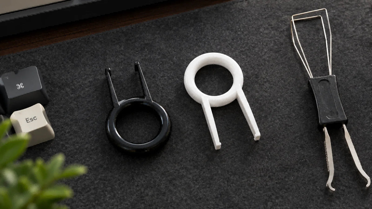 Three ring-style keycap pullers and two loose keycaps on a gray mat.